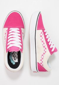 Vaaleanpunaiset ja kermaiset Vans-tennarit, joissa on valkoiset nauhat, ruudulliset yksityiskohdat ja teksturoitu kangaspinta. Pyöreä kärki ja litteä pohjarakenne.