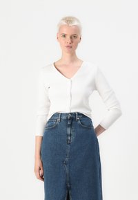 Hvit ribbestrikket langermet cardigan med V-hals og knappelukking, sammen med et blått denimskjørt med sliss foran og høy midje.