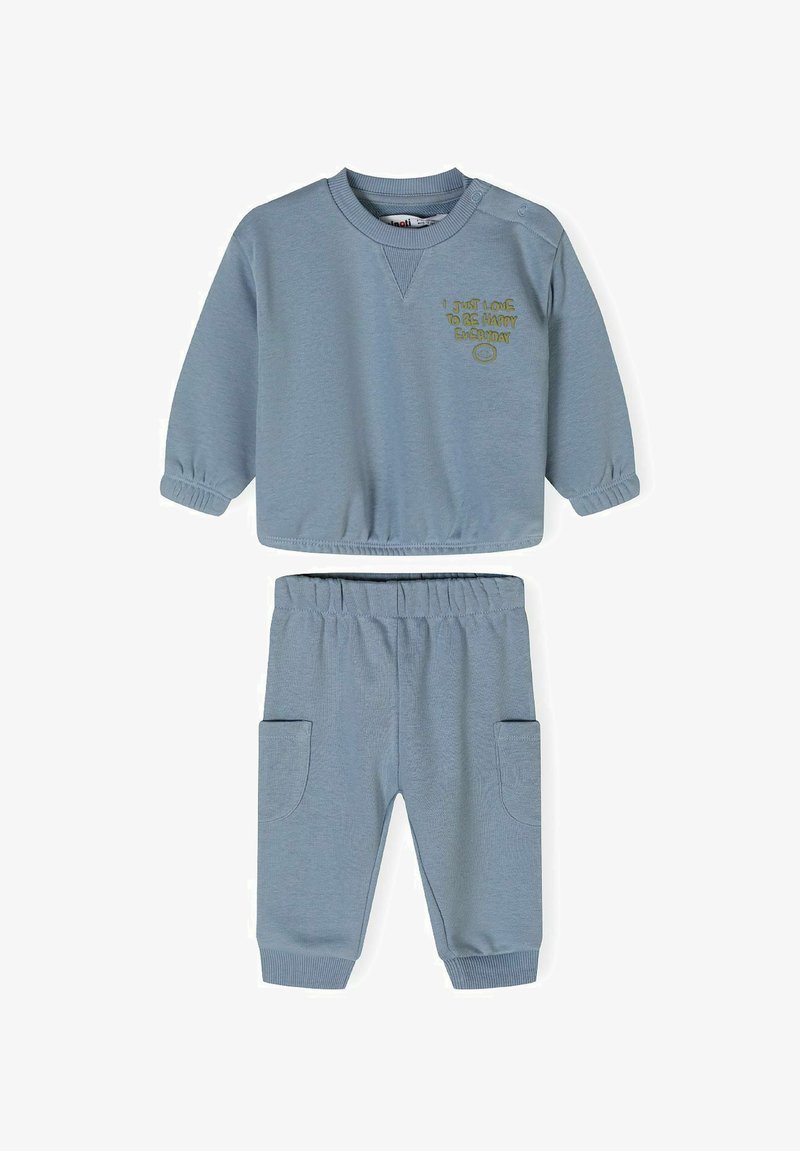 Gaiši zils džemperis un saskaņotas bikses. Džemperim ir ribotas piedurknes un noapaļots kakls, ar izšūtiem uzrakstiem. Biksēm ir sānu kabatas.