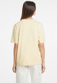 Jasnożółta, krótka koszulka z luźnym krojem, wykonana z miękkiej bawełny. Posiada klasyczny okrągły dekolt i prosty, ściegowany brzeg.