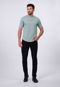 Camiseta verde menta de manga corta con un texto en negro en el pecho, combinada con unos vaqueros negros que tienen acentos de canalé.