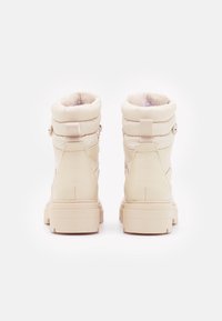 Bottines beiges à tige matelassée et doublure en fausse fourrure, avec deux boutons et une semelle épaisse pour une meilleure adhérence.