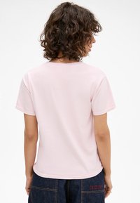 Pink short-sleeve t-shirt with a round neck and a smooth texture. The back is plain with a slight curved hem. Positioned against a neutral background.
