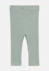 Leggings per bambini di colore verde chiaro a coste morbide, con una fascia elastica in vita, esposti in piano su uno sfondo bianco.