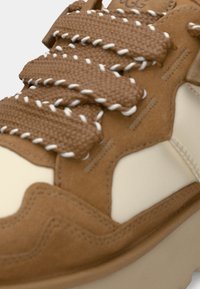 Brune semsket og kremfargede sneakers med strukturert stoff, tykke snørebånd med hvite detaljer, og en konturert såledesign.
