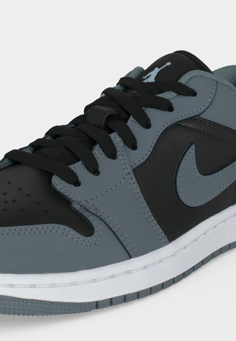 Niedriger Sneaker mit schwarzen und grauen Lederpanelen, schwarzen Schnürsenkeln, grauem Nike-Swoosh und Jumpman-Logo auf der Zunge, auf einer weißen Sohle.