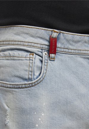 Vaaleansiniset farkut, joissa etutasku, pieni kulutusefekti ja punainen suorakulmainen lappu vyölenkissä, yhdistetty mustaan ribbineulottuun yläosaan.