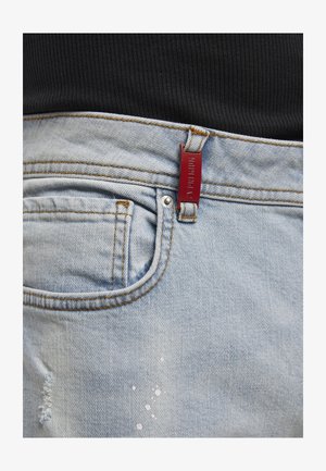 Vaaleansiniset farkut, joissa etutasku, pieni kulutusefekti ja punainen suorakulmainen lappu vyölenkissä, yhdistetty mustaan ribbineulottuun yläosaan.