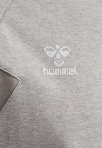 Logo avec une abeille stylisée et le texte « hummel » imprimé en blanc sur fond de tissu gris clair.