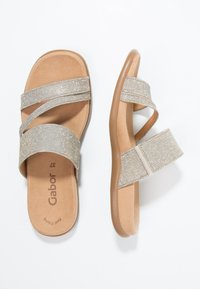 Sandales argentées à bride croisée avec une semelle intérieure rembourrée et une semelle en caoutchouc beige. Les brides ont une texture douce avec un léger brillant.