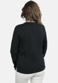 Camiseta negra de manga larga con escote redondo, hecha de tejido suave. Presenta aberturas laterales en el dobladillo y un diseño de corte recto.