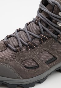 Gros plan sur une botte de randonnée gris foncé avec tissu texturé, surpiqûres en daim, oeillets renforcés et lacets ronds gris noués en motif croisé.
