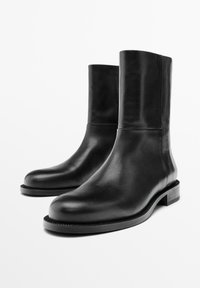 Bottines en cuir noir avec un design épuré, un bout rond et un talon bas empilé. Texture lisse et silhouette minimaliste.