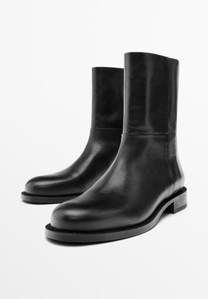 Zwarte leren enkelboots met een strak ontwerp, ronde neus en een lage gestapelde hak. Gladde textuur en minimalistische silhouet.