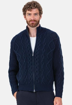 Navy knitted cardigan with a high collar, front zipper, and textured cable patterns throughout. Ribbed cuffs and hem.