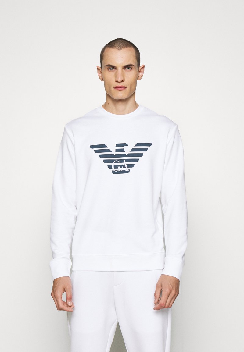 Sweatshirt blanc avec un logo graphique en marine. Fabriqué en tissu doux, avec des manches longues et des poignets côtelés. Design simple à col rond.