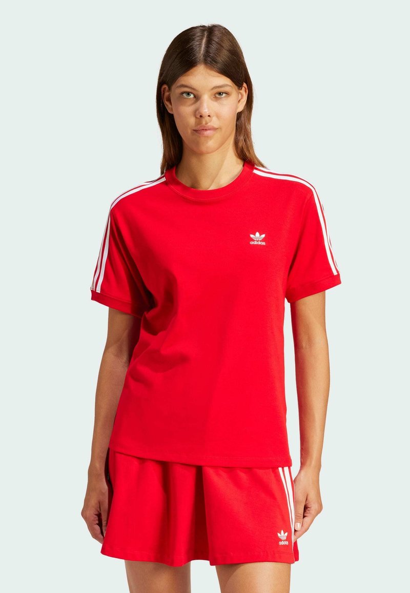 Rød bomulds t-shirt med hvide tre-stribe detaljer på ærmerne og lille hvidt logo på brystet, parret med en matchende rød nederdel.