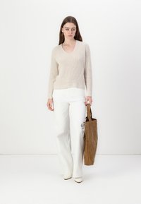 Pull en tricot côtelé beige avec col en V, associé à un pantalon large blanc et un tote bag marron. Cet article présente un design épuré et une texture subtile.