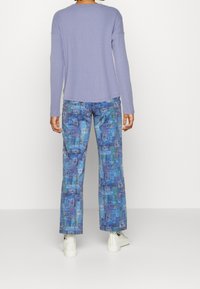 Ljust lila långärmad topp kombinerad med blå mönstrade vida byxor med abstrakta mönster och vita skor med en diskret logotyp.