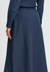 Jupe rayée bleu marine en tissu lisse, dotée d'une ceinture élastique et de détails de poignet boutonné sur la manche, présentée de dos.