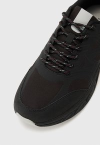 Black athletic shoe featuring a mesh upper, reinforced toe cap, textured side panels, and contrasting multi-colored laces.