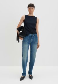 Top senza maniche a costine blu navy abbinato a jeans dritti di jeans di lavaggio medio e scarpe nere con punta affusolata. La modella tiene una borsa nera dal design tessurizzato.
