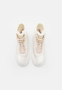 Zapatillas altas blancas con una textura brillante, que presentan cordones beige, herrajes dorados y un suave forro interior.