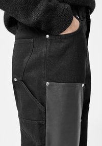 Schwarze Denim-Hosen mit seitlichem Einsatz aus schwarzem Leder, silbernen Druckknöpfen und mehreren Taschen für Funktionalität.