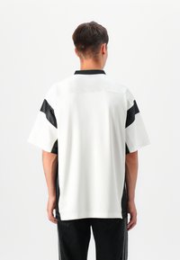 Short-sleeve shirt with a white body, black accents on shoulders and sides, and a collar. Features a textured fabric and side slits.