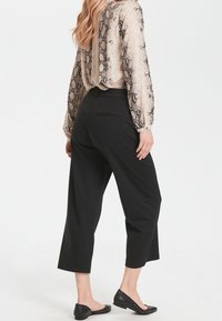 Černé zkrácené kalhoty s bočními kapsami, které jsou kombinovány s béžovou blůzou s hadím vzorem, dlouhými rukávy a designem s V-výstřihem na zádech.