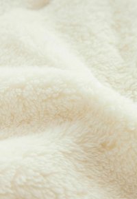 Couverture douce de couleur crème avec une surface texturée et moelleuse, présentant des fibres duveteuses et un drapé uniforme et lisse.