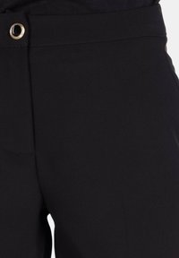 Pantaloni neri con una texture liscia, dotati di occhiello metallico in vita e una vestibilità sartoriale senza tasche visibili.