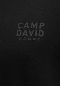 Black textured fabric with "CAMP DAVID" and "SPORT" printed in a slightly lighter shade, centered on the material.