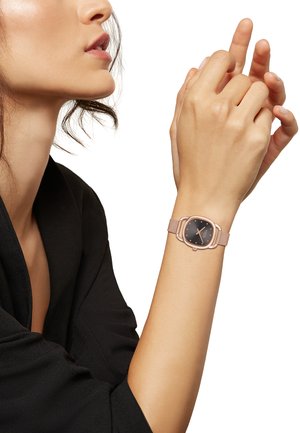 Montre en or rose avec un cadran carré, un fond noir et un bracelet en mesh. Le design présente des bords arrondis et des marquages horaires minimalistes.