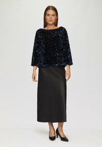Czarna top z cekinami i długimi rękawami, w połączeniu z elegancką satynową spódnicą w kolorze czarnym oraz czarnymi szpilkami. Prosty design, błyszczące tekstury.