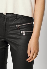 Pantalones de cuero sintético negros con dos bolsillos frontales con cremallera plateada. La tela tiene una textura lisa y brillante.