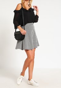Blusa nera senza spalle con dettagli a volant, abbinata a una gonna a righe bianco e nero e sneakers bianche, mentre porta una piccola borsa a tracolla nera.
