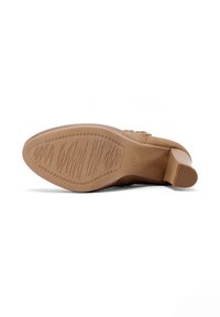 Bota de tacón beige tumbada de lado que muestra la suela texturizada y el tacón bloque sobre un fondo blanco.