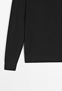 Pull noir en tricot avec manches longues, présentant une texture côtelée et un ourlet côtelé. Design simple, sans motifs ni éléments visibles.