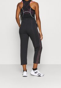 Frau trägt schwarze verkürzte Sporthosen mit roten Details, ein schwarz-pinkes Sport-Tanktop und weiße Nike-Sneaker mit schwarzen Socken.