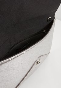 Sac à main pailleté argenté au design épuré, avec un intérieur en tissu noir et une poche zippée pour le rangement. Fermeture par pression magnétique à l'avant.