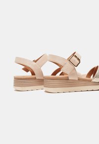 Sandales en suede beige avec un talon compensé, sangle ajustable avec boucle et détails texturés sur le devant. Doublure intérieure lisse.