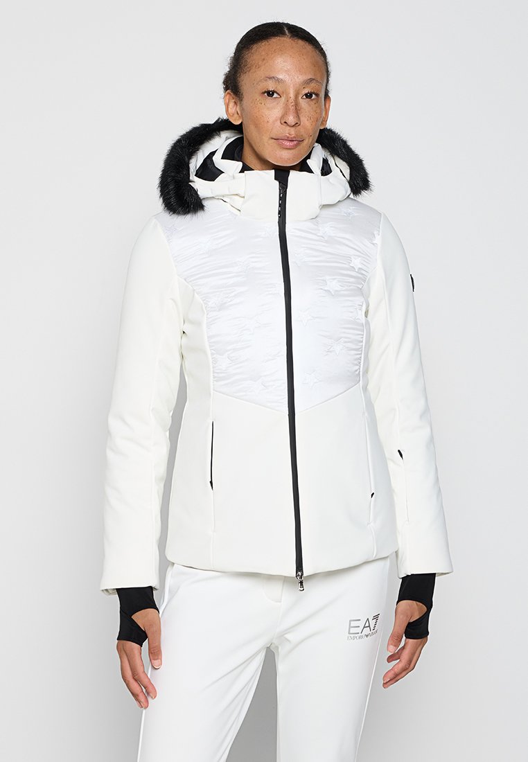 Giacca bianca con un pannello superiore lucido e testurizzato e un bordo in pelliccia sul cappuccio. Presenta una zip frontale e tasche laterali, con dettagli neri.