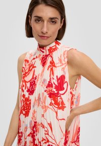 Robe sans manches plissée avec un col haut, présentant un motif floral en rouge, rose et bleu clair sur un fond clair. Tissu léger.