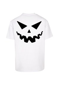 Hvid t-shirt med et stort sort grafisk motiv af et stiliseret, takkete smiley-ansigt med skarpe øjne og et tandrigt smil på ryggen.