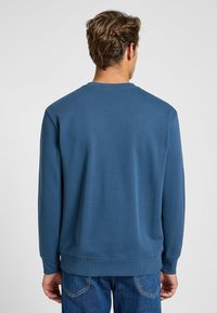 Sudadera de cuello redondo en mezcla de algodón azul, con mangas largas, puños y dobladillo acanalados, con una textura suave y detalles de diseño mínimos.