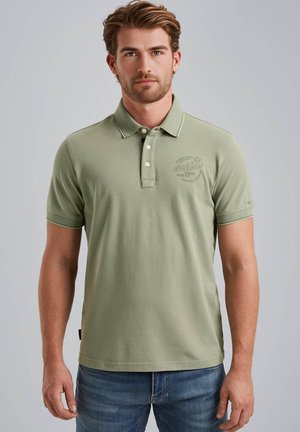 Polo shirt vert clair avec trois boutons, manches courtes et un logo discret sur la poitrine ; fabriqué en coton texturé.