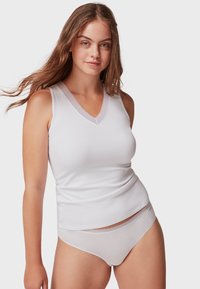 Camiseta sin mangas blanca con escote en V y detalles de encaje, combinada con braguitas blancas a juego. Tejido suave con un diseño ajustado.