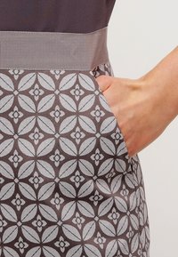 Bruin patroon kledingstuk met een grijs bloemontwerp, voorzien van een textuurbund en een zijzak die in de stof is geïntegreerd.