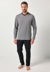 Szara prążkowana bluzka z długim rękawem z czarnym dekoltem w kształcie litery V, w połączeniu z czarnymi spodniami. Tkanina wydaje się miękka i lekka. Stopy są boso.